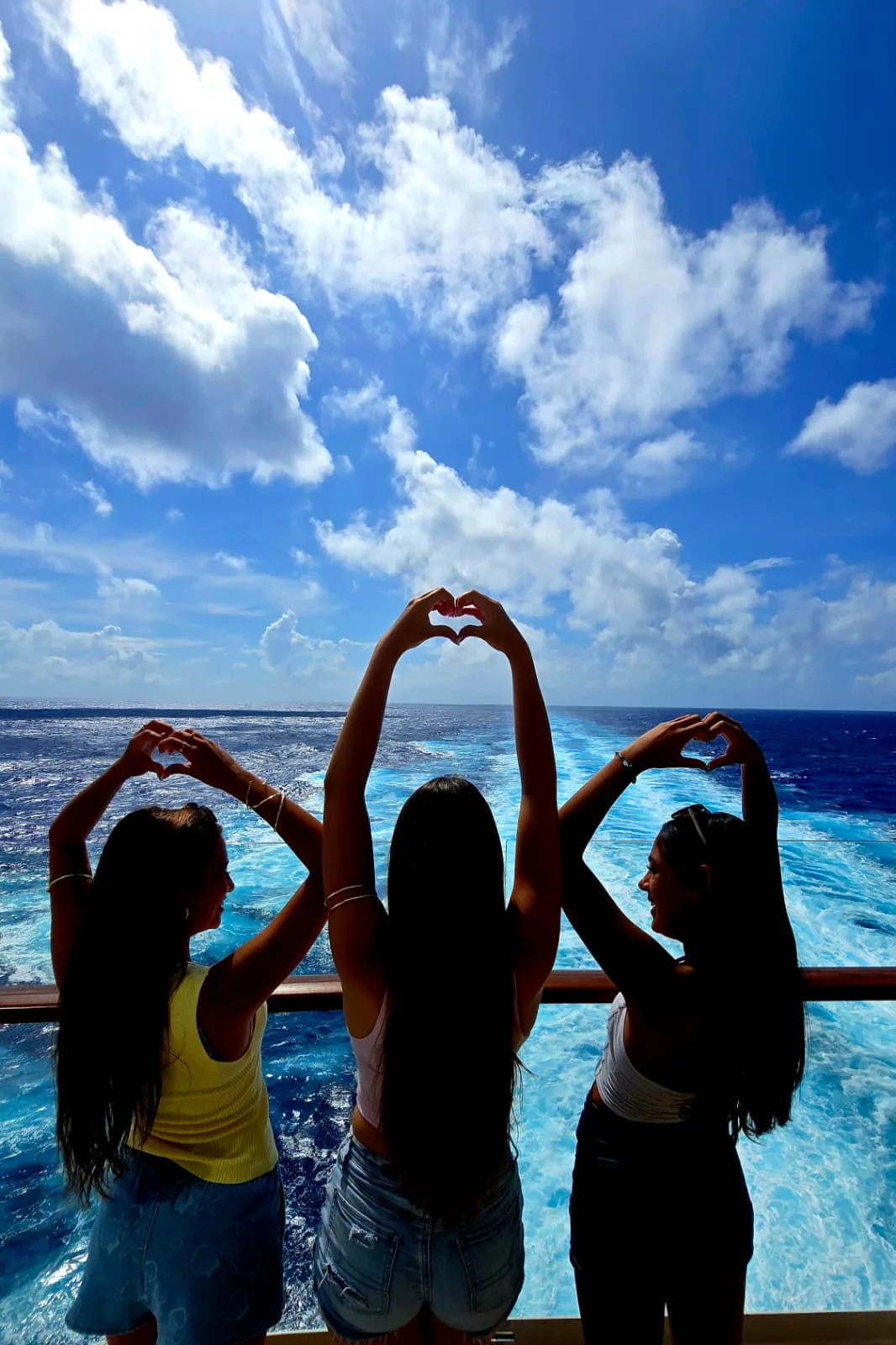 Friends making heart shapes with their arms by the sea
