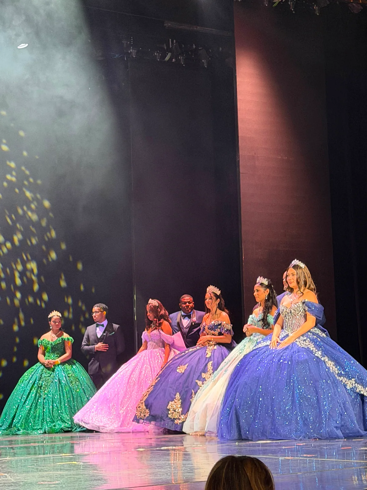 Quinceañeras in colorful dresses during a stage celebration