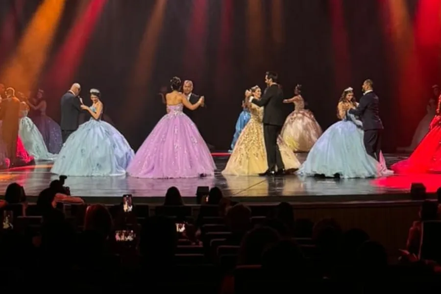 Quinceañeras dancing with their fathers under colorful gala lights