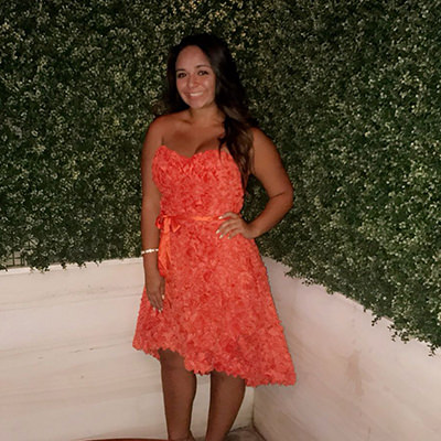 Wearing a coral dress in front of a green hedge.