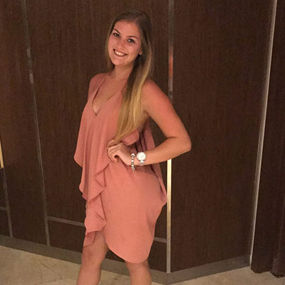 Standing in a coral dress in front of wood panels.
